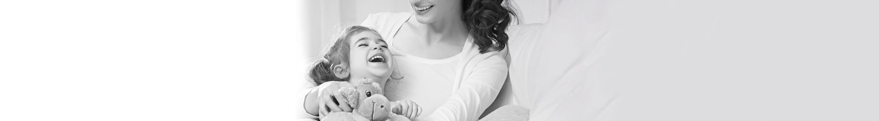 Little girl lying in mother´s arm, laughing and holding a stuffed animal.
